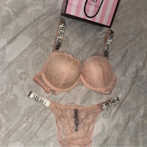 Rosa spetsunderkläder från Victoria’s secret  - Snyggt set med rosa spetsunderkläder från Victoria's Secret. BH:n har vadderade kupor och axelband med glittriga paljettdetaljer. Trosorna matchar med samma spets och rhinestones på banden. Bh-n är storlek 75 C och trosorna är i storlek M men passar även S