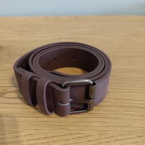 Brunt skärp med silverfärgat spänne - Snyggt brunt skärp i skinn med ett stilrent silverfärgat spänne. Perfekt för att komplettera din outfit med en klassisk touch. Skärpet har flera hål för justerbar passform.