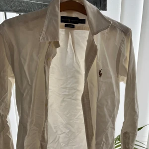 Vit skjorta från Ralph Lauren - Säljer en stilren vit skjorta från Ralph Lauren i slim fit. Skjortan har långa ärmar och en klassisk krage. Den är broderad med den ikoniska logotypen på bröstet. Perfekt för en elegant look.