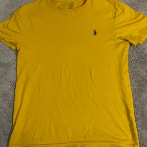 Gul t-shirt från Ralph Lauren - Säljer en gul t-shirt från Ralph Lauren med en liten blå broderad logga på bröstet. Perfekt om man ska på en Sverige match☺️ passar storlek S med