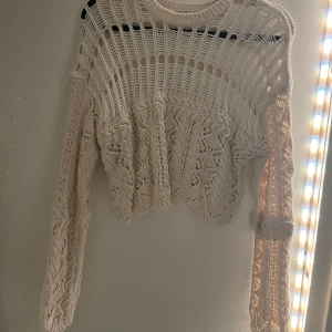 Vit stickad tröja från Zara - Säljer en vit stickad tröja från Zara med ett unikt mönster och croppad design. Tröjan har långa ärmar och en luftig stickning som ger en bohemisk känsla. Perfekt för lager-på-lager-stil eller som statement-plagg. 🌟