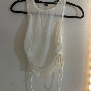 Vit linnetopp från Stronger - Säljer en snygg vit linnetopp från Stronger. Toppen har en stilren design med dragsko-detaljer på sidan för en justerbar passform. Perfekt för träning eller en avslappnad dag.