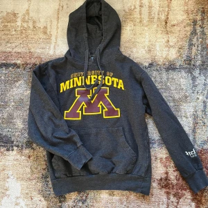 Mörkgrå hoodie vintage med tryck - Säljer en mörkgrå hoodie med tryck från University of Minnesota. Den har en stor ficka fram och justerbar huva. Perfekt för en avslappnad stil.