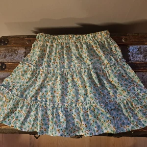 Blommig kjol från Shein - Charmig blommig kjol från Shein i grönt och gult. Kjolen har en volangdesign som ger en lekfull känsla. Perfekt för varma dagar med sitt lätta och luftiga material.