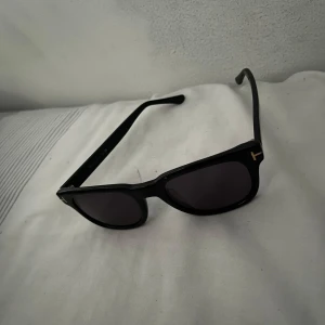 solglasögon Tom Ford - Snygga svarta solglasögon från Tom Ford med en klassisk rektangulär form. De har mörka linser och en subtil logotypdetalj på skalmen. Perfekta för en stilren look. NY PRIS RUNT 3000, priset är ej hugget i sten så kom med BUD FÖRSLAG BYTE FUNKAR OCKSÅ!