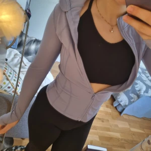 Ljuslila träningsjacka med dragkedja - Säljer en snygg ljuslila träningsjacka med dragkedja. Jackan har en tight passform och långa ärmar, perfekt för träning. Den är tillverkad i ett syntetmaterial som andas och ger bra rörelsefrihet. Helt oanvänd!