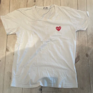 Comme des Garçons Play  - Säljer en stilren vit t-shirt från Comme des Garçons Play med ett ikoniskt rött hjärta på bröstet. Perfekt för en casual look. T-shirten har en klassisk passform och är kortärmad.