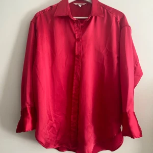 Rosa satinblus - Snygg rosa blus i satin med klassisk krage och knappar framtill. Blusen har långa ärmar och en elegant glansig yta som ger en lyxig känsla. Perfekt för att lyfta vilken outfit som helst.