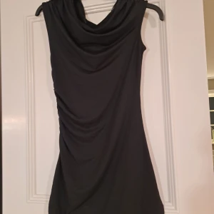 Svart klänning från H&M Divided - Snygg svart klänning från H&M Divided i återvunnen polyester. Klänningen har en draperad design och är ärmlös, vilket ger en elegant look. Perfekt för olika tillfällen.