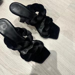Svarta klackskor med flätad rem från H&M - Snygga svarta klackskor från H&M med en unik flätad remdesign. Skorna har en fyrkantig tå och en elegant klack som ger en stilren look. Perfekta för att lyfta vilken outfit som helst.