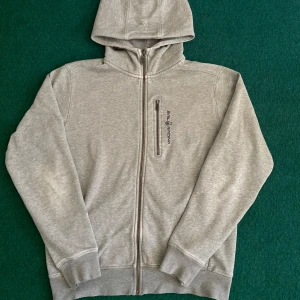Grå hoodie från Sail Racing - Säljer en stilren grå hoodie från Sail Racing med dragkedja och en praktisk bröstficka. Perfekt för kyliga dagar med sin mjuka och bekväma passform. Huvan ger extra värme och stil. Passar både till vardags och mer avslappnade tillfällen. Tröjan är använd med några defekter, bland annat en jätte liten fläck som inte ens syns. Armbågen är lite sliten men syns knappt det med, dock är ärmen lite slitna! Pris kan diskuteras 