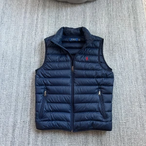 Mörkblå dunväst från Polo Ralph Lauren - Säljer en snygg mörkblå dunväst från Polo Ralph Lauren. Fint skick med små tecken på användning där va priset! Storlek S