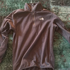 Svart fleece tröja från The North Face - Säljer en svart fleece tröja från The North Face med halv dragkedja och hög krage. Perfekt för kyliga dagar och utomhusaktiviteter. Tröjan har långa ärmar och är supermjuk och bekväm. Passar bra för lager-på-lager stil.