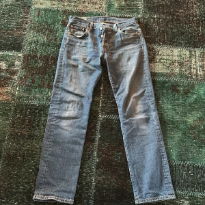 Levis 501 jeans - Klassiska Levis 501 jeans i blå denim. De har en rak passform och knappar i gylfen. Perfekta för en tidlös stil. Storlek W30 L32