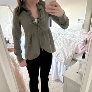 Grön blus med volangdetaljer - Snygg grön blus med volangdetaljer och knytning framtill. Helt ny med lappar kvar 