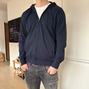 Mörkblå hoodie med dragkedja - Säljer en stilren mörkblå hoodie med dragkedja. Perfekt för en avslappnad look. Tröjan har långa ärmar och en bekväm passform.