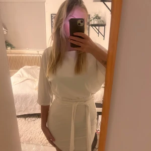 Vit klänning med knyte - Helt ny med prislapp och i orginalförpackning, vit klänning med trekvartsärm och knytband i midjan. Perfekt som studentklänning men även till annat. Kostar 500kr på hemsidan och aldrig använd