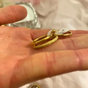 Guldiga örhängen - Snygga guldiga ring med en glittrig yta. Perfekta för att ge en touch av glamour till din outfit. De är runda och har en elegant design som passar till många tillfällen.