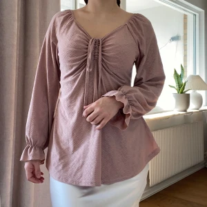 Rosa blus med knytning - Säljer en söt rosa blus med knytning framtill och långa ärmar. Blusen har en lätt volangdetalj vid ärmsluten och en fin struktur i tyget. 