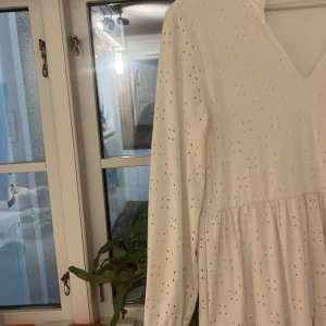 Vit klänning med broderade detaljer från Vila - Säljer en vacker vit klänning från Vila med broderade detaljer och v-ringning. Klänningen har långa ärmar och ett luftigt fall, perfekt för vår och sommar. Den är tillverkad i ett lätt och bekvämt material. Den har en liten fläck som jag tror går bort i tvätten, använd två ggr perfekt för tex student elle en varm sommardag, pris kan diskuteras