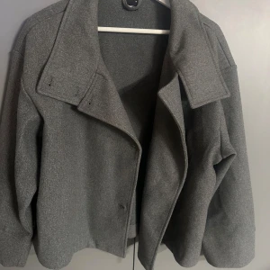 Grå kappa med krage -  Grå kortare kappa med bred krage. 