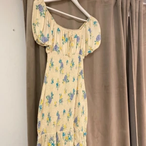 Blommig klänning från BikBok - Charmig blommig klänning från BikBok i ljusgul nyans med blå och lila blommor. Klänningen har korta puffärmar och en smickrande passform. Perfekt för sommarens alla tillfällen!