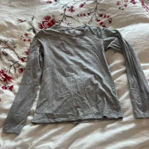 Grå långärmad tröja - Säljer en enkel och bekväm grå långärmad tröja. Perfekt för lager-på-lager under kyligare dagar. Tröjan har en rund halsringning och är tillverkad i ett mjukt material.