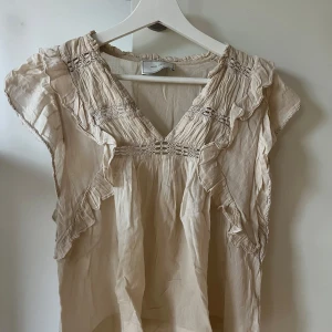 Beige blus med volang från Neo Noir - Supersöt beige blus från Neo Noir i luftigt och lätt material, perfekt för varmare dagar. Säljes nu i storlek S ✨