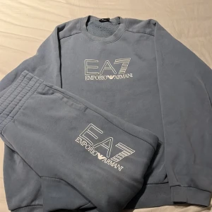 Blå EA7 Emporio Armani sweatshirt - Säljer en stilren blå sweatshirt från EA7 Emporio Armani med stort vitt logotryck på bröstet. Tröjan har rund halsringning och långa ärmar, tillverkad i mjuk bomull för maximal komfort. Perfekt för dig som gillar exklusiva streetwear-vibbar.