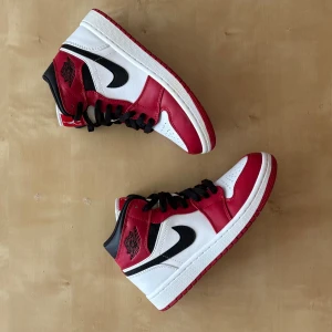 Nike Air Jordan 1 Chicago Mids  - Säljer ett par ikoniska Nike Air Jordan 1 Highs i Chicago-färg. Skorna har vit och röd ovandel i skinn med svarta detaljer och svart swoosh. Klassisk hög siluett, svart snörning och röd yttersula. Perfekta för dig som vill sticka ut med en tidlös sneaker.