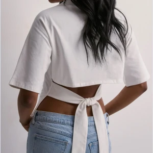 Vit  topp med knyt i ryggen - Säljer denna populära tröjan från Nelly då jag inte fått användning av den. Tröjan är i jätte bra skick så jag aldrig använt den. Skriv för fler bilder. 