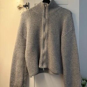 Grå stickad kofta med dragkedja - Mysig grå stickad kofta med hög krage och hel dragkedja framtill. Tröjan har en ribbad struktur och långa ärmar, perfekt för kyliga dagar. Enkel att matcha och superbekväm att bära. Från bikbok 