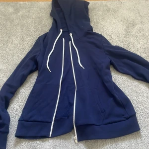 Mörkblå hoodie från Even&Odd - Mörkblå hoodie från Even&Odd med dragkedja framtill och vita snören i huvan. Tröjan har långa ärmar, två fickor och är tillverkad i mjuk bomullsmix. Perfekt för chill dagar eller när du vill ha en enkel och stilren look.