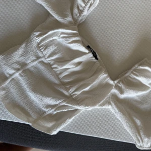 Vit omlott blus från Gina Tricot - Supersöt vit omlott blus från Gina Tricot i storlek S. Toppen har puffiga korta ärmar och en lätt skrynklig struktur i tyget.