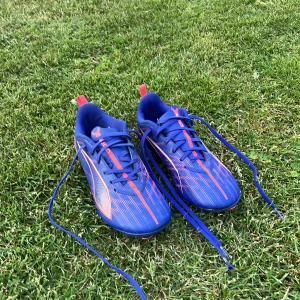 Blå fotbollsskor från Puma ordinarie pris 700 SEK - Säljer ett par blå fotbollsskor från Puma med stiliga orangea detaljer. Jag säljer dem för att jag vuxit ur dem. Men dock så är de lite slitna längst fram på skon och dobbarna är något nerslipade men bara några dobbar på skon är det men de funkar ändå hur bra som helst och de kommer säkert att göra det ett tag till (typ ett år), men snörena är också lite slitna men de går att byta ut hur enkelt som helst. Prisförslag och andra frågor svaras. Till sist så är de köpta på en JD butik i London.