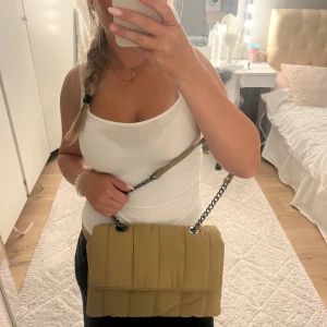 Beige quiltad axelväska från Zara - Säljer en beige quiltad axelväska från Zara med kedjerem och mjukt tyg. Väskan har ett stort fack och en innerficka med dragkedja. Perfekt storlek för det viktigaste och snygg att bära crossbody eller på axeln.
