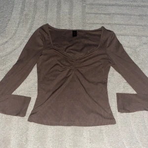 Brun ribbad långärmad topp - Säljer en brun långärmad topp med ribbad struktur och snygg v-ringning med rynkdetalj framtill. Perfekt för dig som gillar en enkel men trendig stil. Passar till både jeans och kjol för en chill look.