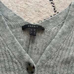 Ljusgrå stickad kofta från Esprit - Mysig ljusgrå stickad kofta från Esprit med stora knappar framtill och v-ringad hals. Koftan har långärmad passform och är perfekt att slänga på sig när det är kyligt. Den är mjuk och har en luftig stickning som ger en chill vibe.