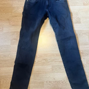 Replay Hyperflex svarta jeans, W30 L30 - Svarta Replay Hyperflex jeans med slim fit och klassisk femficksdesign. Jeansen är stretchiga och sitter tajt längs benen. Perfekta om du gillar en modern och stilren look. Materialet är mjukt och följsamt för extra komfort.