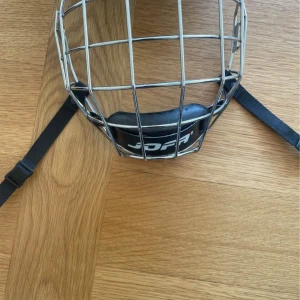 Jofa galler medium - Säljer ett klassiskt hockeygaller från Jofa i silverfärgad metall med svart hakskydd och justerbara svarta remmar. Perfekt för dig som vill skydda ansiktet på isen och samtidigt ha bra sikt. Passar de flesta hjälmar.