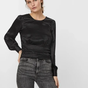 Svart glansig blus med v-ringning - Säljer en supersnygg blus/festtopp från Vero Moda i glansigt satinliknande material. V-ringad rygg, markerad midja och puffärmar. Den går att bära åt båda hållen och har endast använt den två gånger då den nu inte passar längre! Upplevs som S/M! Nypris 430kr men säljer för 200kr