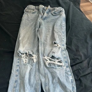 Ljusblå ripped jeans från Gina Tricot - Säljer ett par ljusblå jeans från Gina Tricot med snygga slitningar och stora hål på båda benen. Klassisk femficksmodell med knapp och dragkedja. Perfekt för dig som gillar en avslappnad och trendig look. 