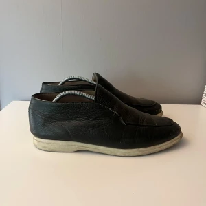 Rose & Born skor - Klassiska svarta loafers i äkta skinn med rund tå och platt sula. Skorna har en stilren design utan snörning och en vit sula som ger en snygg kontrast. Perfekta för dig som gillar en clean och tidlös look. Tillkommer box och påse