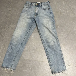 Blå raka jeans från Zara, strl 34 - Snygga blå jeans från Zara i rak modell med hög midja. Jeansen har klassisk femficksdesign, slitna benslut och ljus tvätt. Perfekta för en avslappnad och trendig look. Tillverkade i bomull för skön känsla.