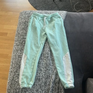 Mintgröna mjukisbyxor från H&M - Snygga mintgröna mjukisbyxor från H&M med vita detaljer längs benen och dragsko i midjan. Byxorna har resår vid benslut och är gjorda i mjukt bomullsmaterial, perfekta för chill dagar eller träning använd ett par gånger.