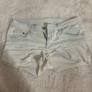 Ljusblåa jeansshorts från &Denim - Snygga ljusblå jeansshorts från &Denim med råa, fransiga kanter och slitningar framtill. Klassisk femficksmodell med knapp och dragkedja. Perfekta för varma dagar och en avslappnad look.