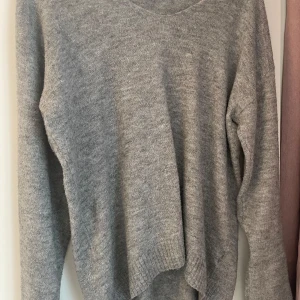 Grå stickad tröja med v-ringning - Mysig grå stickad tröja med v-ringad hals och långa ärmar. Tröjan har en enkel och clean look med ribbade muddar vid ärmslut och nederkant. Perfekt för lager-på-lager och chill dagar.