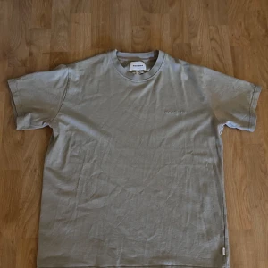 Beige t-shirt från Woodbird - Snygg beige t-shirt från Woodbird i mjuk bomull. Klassisk passform med rund hals och korta ärmar. Diskret broderad logga på bröstet. 