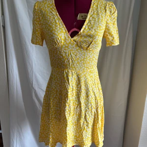 Gul blommig kortklänning från SHEIN - Superfin gul kortklänning från SHEIN med vita blommor, v-ringning och korta ärmar. Klänningen har en figurnära midja, dragkedja i sidan och lätt utställd kjol. Perfekt för sommarens alla tillfällen. Materialet är mjukt och svalt.