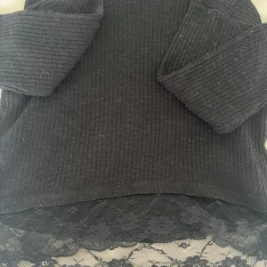 Svart ribbad tröja med spetsdetalj - Svart ribbad tröja med lång ärm och snygg spetskant nertill. Tröjan har en fin passform och är perfekt för dig som gillar en stilren look med en twist. Spetsen ger en extra touch och gör tröjan unik. Superfin att matcha med jeans eller kjol. Köpt på second hand men aldrig använd. 